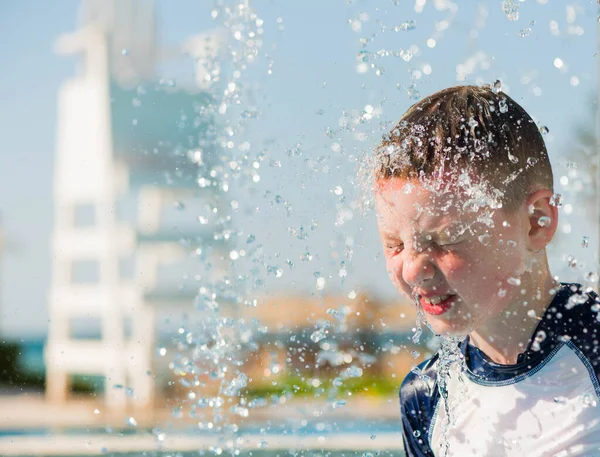 caucasian boy putting head under fountain splash at summer pool playground