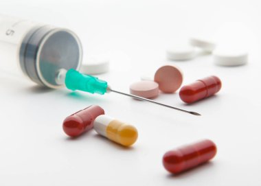 İğne şırınga ve beyaz zemin üzerine hap. İğne ucu odak.