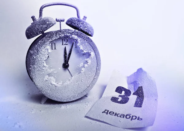 Snow-covered alarm clock and crumpled sheet of tear-off calendar with the date December 31