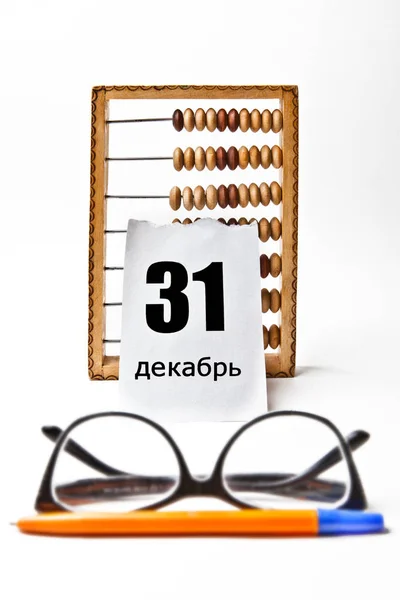 日期为12月31日的日历页 用俄文书写 附有木制账单 贴在眼镜和钢笔旁边 白色背景 — 图库照片