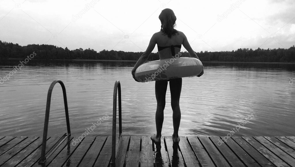 Young teen girl with water wheel ready for swimming on the lake at evening, black and white picture