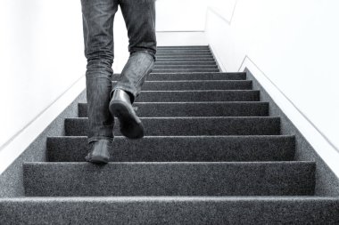 Black and white low angle picture of one man walking upstairs on staircase indoors clipart