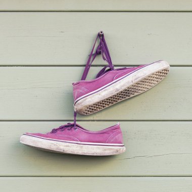 Pair of red old wornout sneakers hanging on the wall clipart
