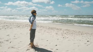 Orta yaşlı bir kadın kumsalda rüzgarlı bir yaz gününde dalgalanan denize bakıyor.