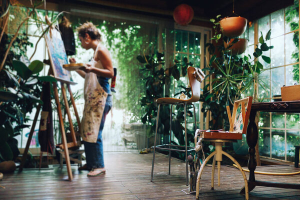 Крытый снимок профессиональной художницы на холсте в студии с растениями
.