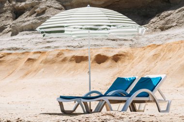 İki güverte sandalyeleri ile bir plaj şemsiyesi yalnız Beach Malta'da yeşil çizgili mavi.