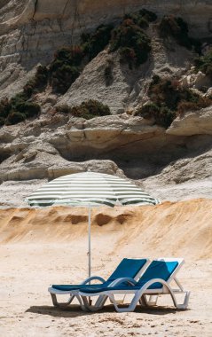 İki güverte sandalyeleri ile bir plaj şemsiyesi yalnız Beach Malta'da yeşil çizgili mavi.