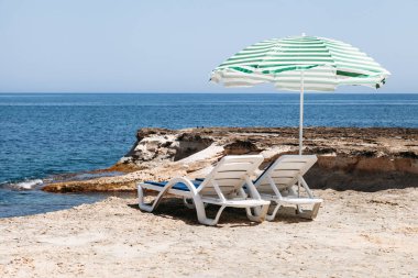 İki güverte sandalyeleri ile bir plaj şemsiyesi yalnız Beach Malta'da yeşil çizgili mavi.
