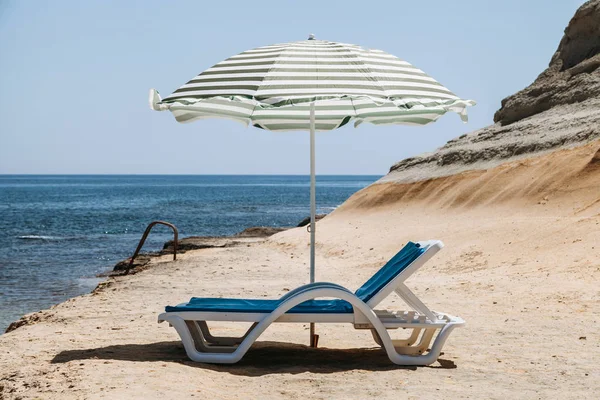 İki güverte sandalyeleri ile bir plaj şemsiyesi yalnız Beach Malta'da yeşil çizgili mavi.