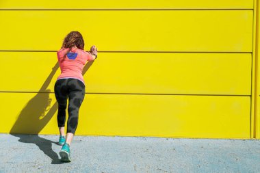 Genç kadın çalıştırmadan önce sarı bir duvara germe