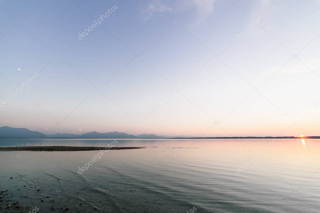 Astronomical conjunction of Sunset in Bavarian lake with moon and sun on sky