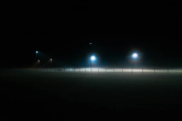 Lonely football field covered by fog at night only illuminated by spotlights