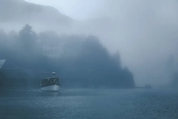 Views of a lonely boat in the fog on the lake Konigsee of Germany with mountains in background