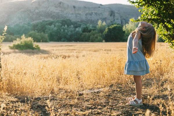 背景の丘とドレスを着てフィールド日没で日光で遊んで金髪少女 — ストック写真