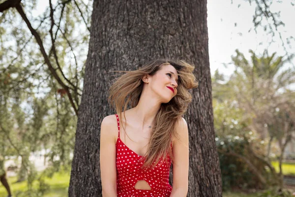 Jeune femme blonde souriante avec robe rouge bougeant ses cheveux — Photo