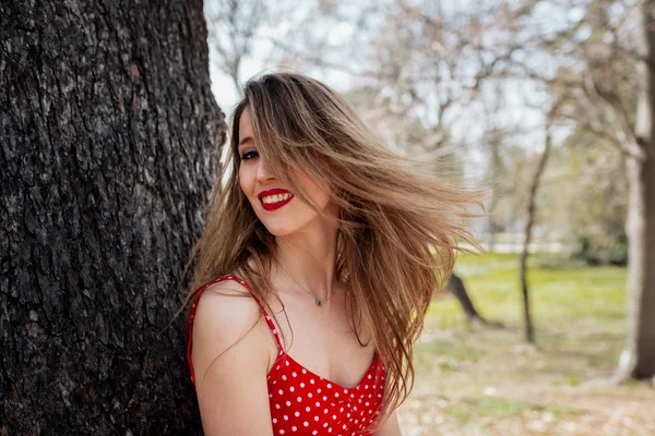 Mladá usměvavá blondýnka s červených šatech pohybuje její vlasy — Stock fotografie