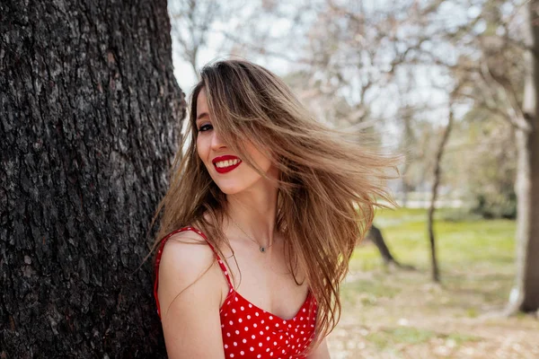 Joven mujer rubia sonriente con vestido rojo moviendo su cabello — Foto de Stock