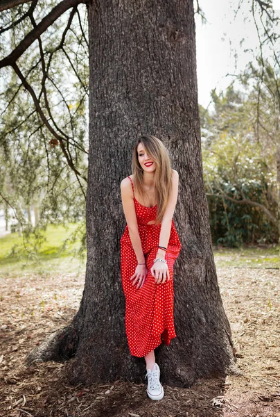 Jeune femme souriante avec robe rouge penchée vers la caméra — Photo
