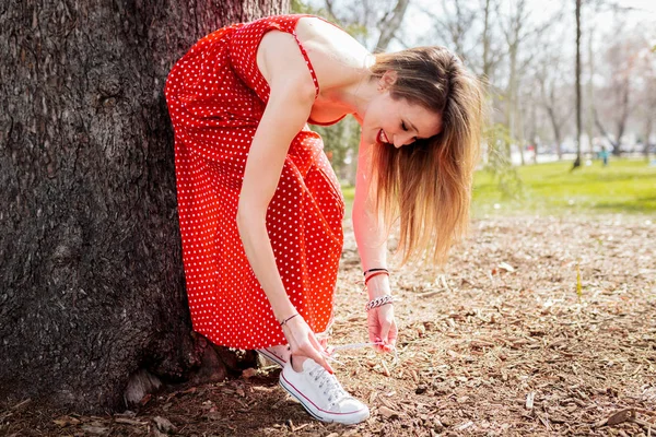 Jonge lachende blonde vrouw leunt koppelverkoop haar sneakers whit jurk — Stockfoto
