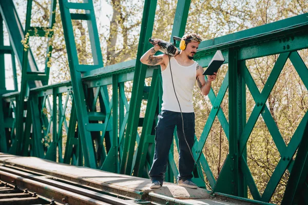 Jovem trabalhador da construção lendo um livro sobre a velha ponte ferroviária — Fotografia de Stock