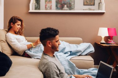 Genç, gülümseyen heteroseksüel çift kanepede birlikte.