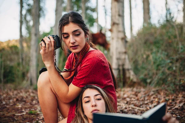 Молодые женщины читают книгу и фотографируют в лесу — стоковое фото