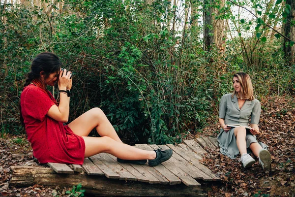 Mujeres jóvenes leyendo un libro y tomando fotos en el bosque — Foto de Stock