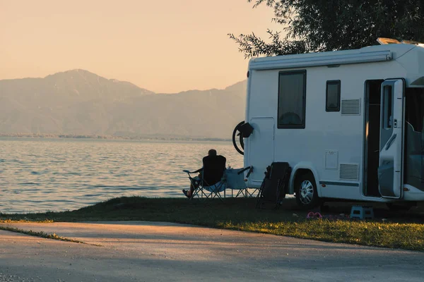 Man sitting near his caravan observes the sunset close the lake — Stock Photo, Image