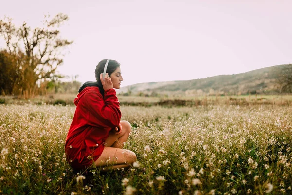 Menina ouvindo música com fones de ouvido sentados entre flores silvestres — Fotografia de Stock