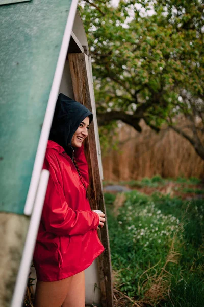 Smiling girl wearing red raincoat takes shelter from the rain — Stock Photo, Image
