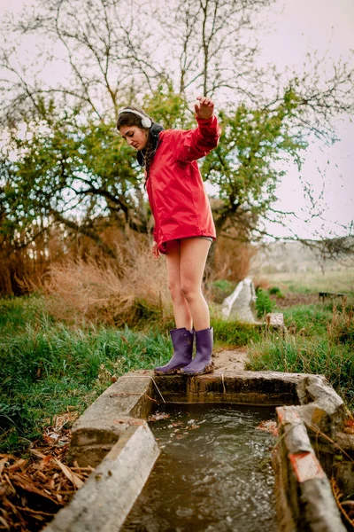 Girl with headphones and raincoat washing her waterproof boots — Stock Photo, Image