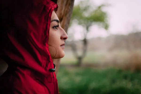 Mädchen in rotem Regenmantel beobachtet den Regen auf dem Feld — Stockfoto