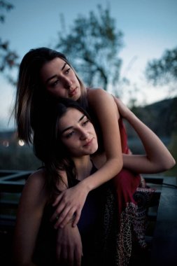 İki genç kadın gün batımı arka plan üzerinde düşünme kucaklayan 