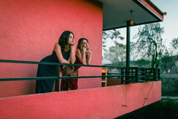 Two young women watch the sunset from their balcony.