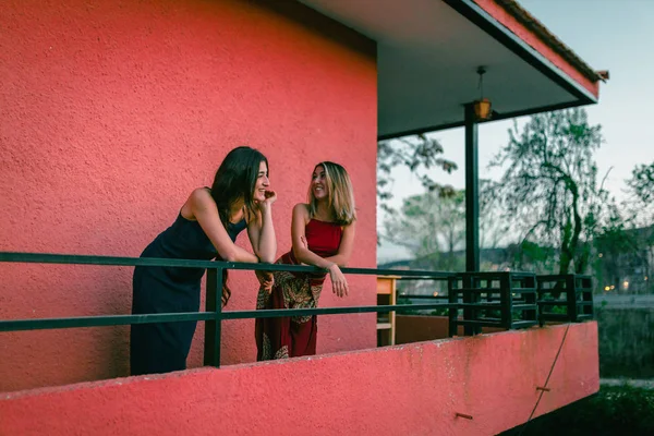 Two young women watch the sunset from their balcony.