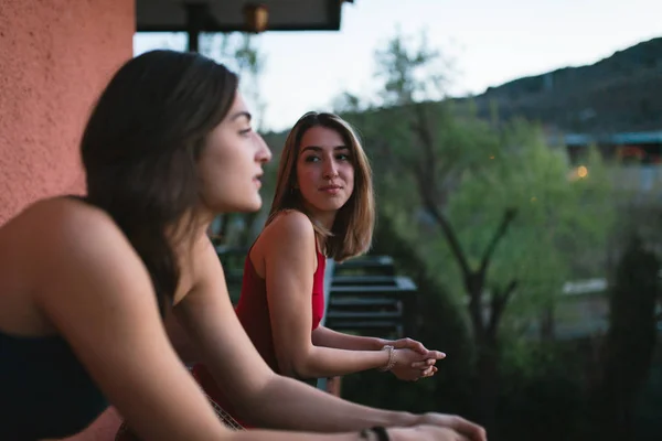 Two young women watch the sunset from their balcony.