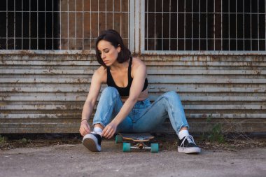 Eski bir sanayi sokağında pateninin üzerinde oturan genç kadın