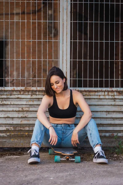 Giovane donna seduta sul suo pattino in una vecchia strada industriale — Foto Stock
