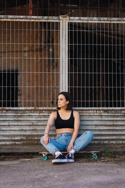Młoda kobieta siedzi na łyżwach w starej ulicy przemysłowej — Zdjęcie stockowe
