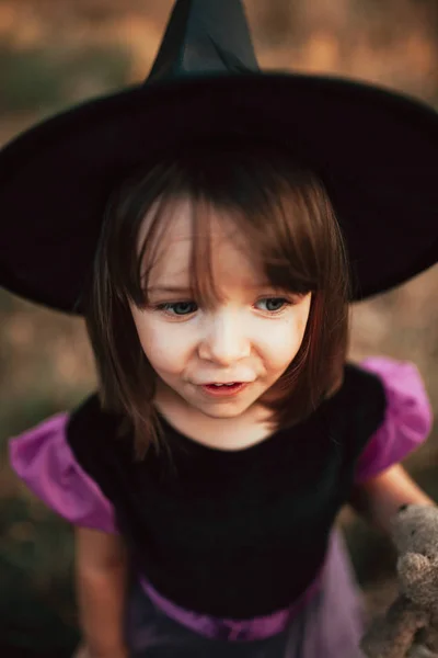 Menina sorridente disfarçada de bruxa na floresta durante o Halloween — Fotografia de Stock