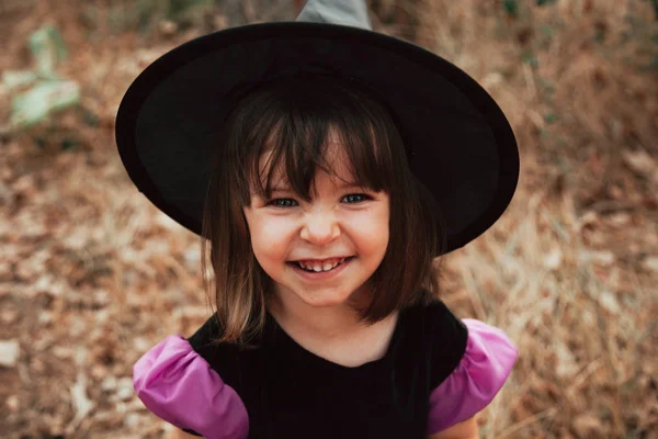 Chica sonriente disfrazada de bruja en el bosque durante Halloween — Foto de Stock