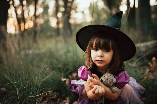 Menina sorridente disfarçada de bruxa na floresta durante o Halloween — Fotografia de Stock