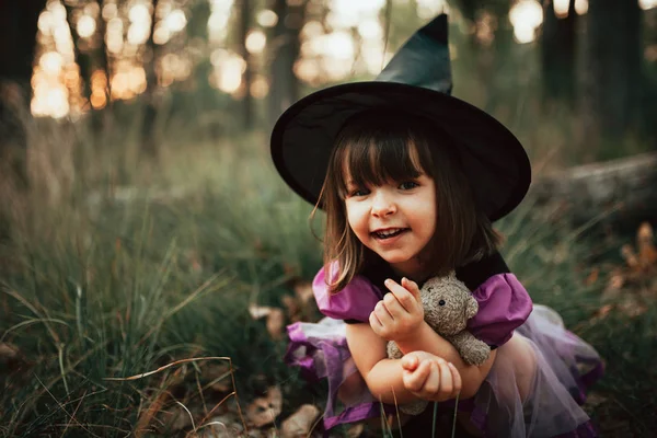 Menina sorridente disfarçada de bruxa na floresta durante o Halloween — Fotografia de Stock