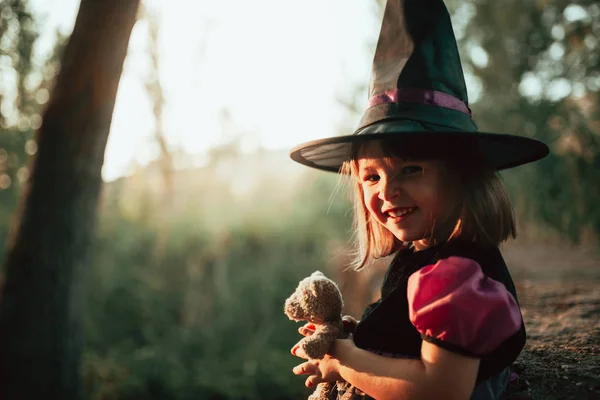 Menina sorridente disfarçada de bruxa na floresta durante o Halloween — Fotografia de Stock