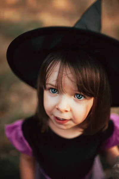 Menina sorridente disfarçada de bruxa na floresta durante o Halloween — Fotografia de Stock