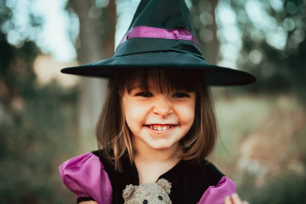 Menina sorridente disfarçada de bruxa na floresta durante o Halloween — Fotografia de Stock