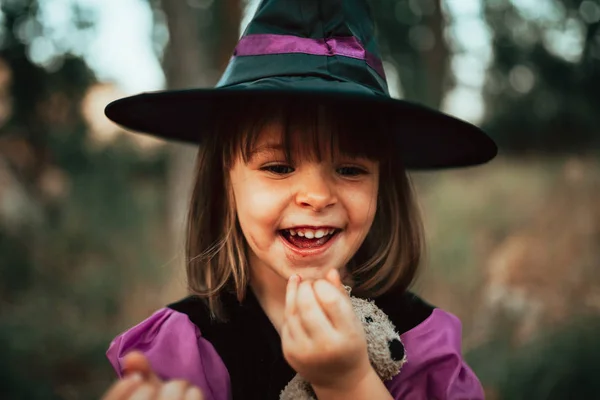 Menina sorridente disfarçada de bruxa na floresta durante o Halloween — Fotografia de Stock