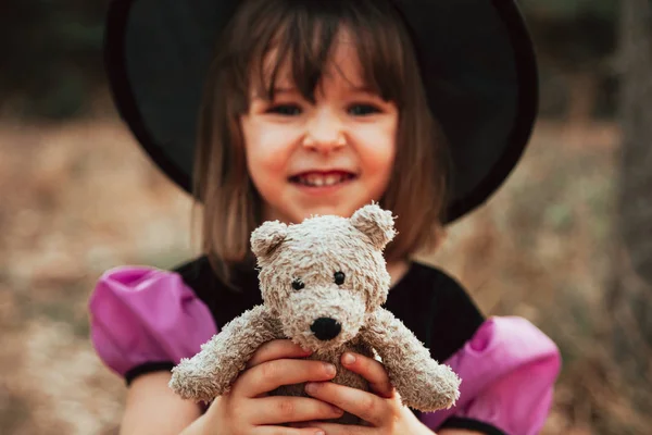 Menina sorridente disfarçada de bruxa na floresta durante o Halloween — Fotografia de Stock