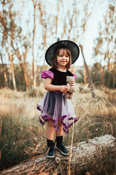 Usmívající se dívka maskovaná jako čarodějnice v lese během Halloweenu — Stock fotografie