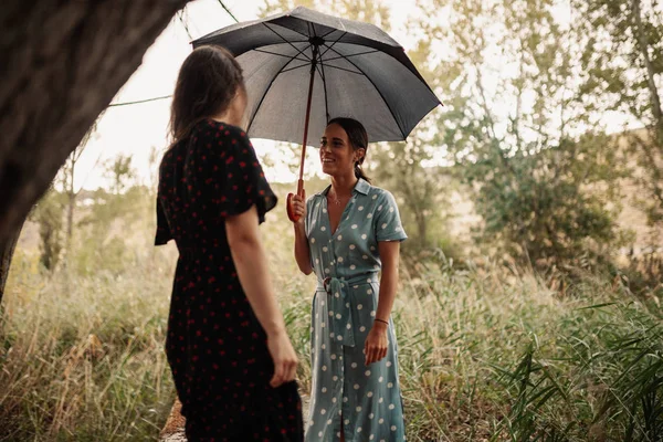 Две молодые женщины стоят с зонтиком на поле — стоковое фото